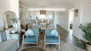 A spacious living room with a sofa, two armchairs, a dining table with chairs, and a kitchen in the background.