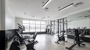 Ein modernes Fitnessstudio mit Cardiogeräten, Gewichtecken und einem großen Spiegel.