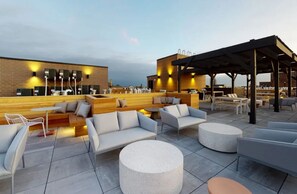 An outdoor seating area with sofas, round tables, and a covered section with umbrellas.