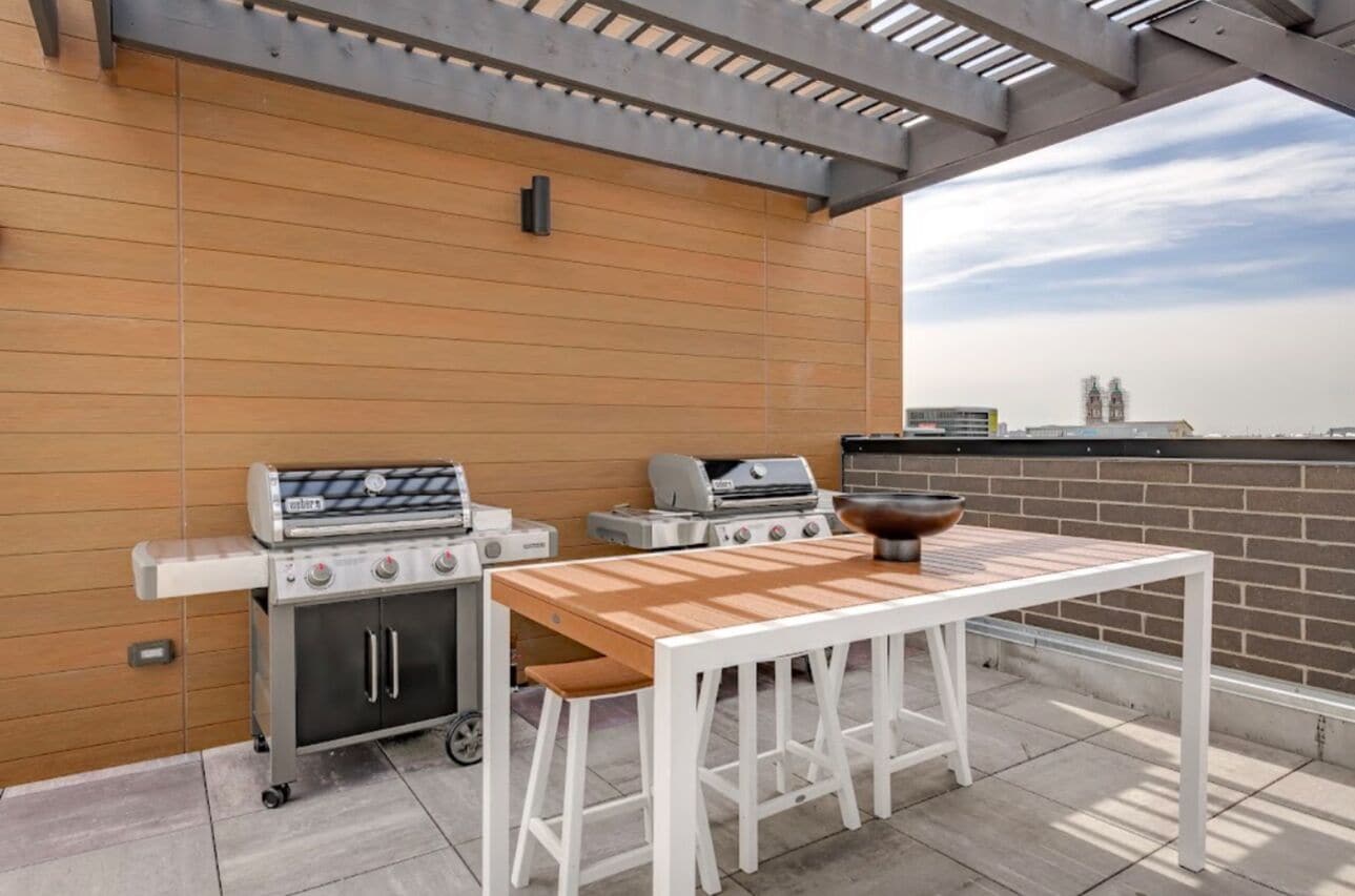 Un patio exterior con una parrilla, una mesa y vistas al horizonte de la ciudad.