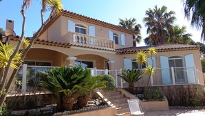 A Mediterranean-style house with a swimming pool, palm trees, and a stone staircase leading to the entrance.