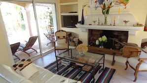 A living room with a white sofa, a glass coffee table, and a fireplace. There are chairs and a TV in the room.