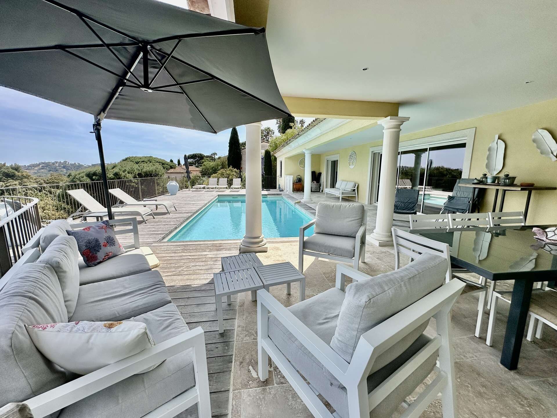A poolside area with white outdoor furniture, a dining table, and a view of the pool.