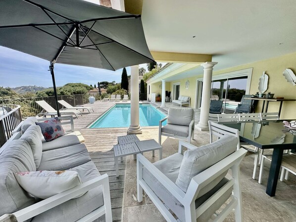 A poolside area with white outdoor furniture, a dining table, and a view of the pool.