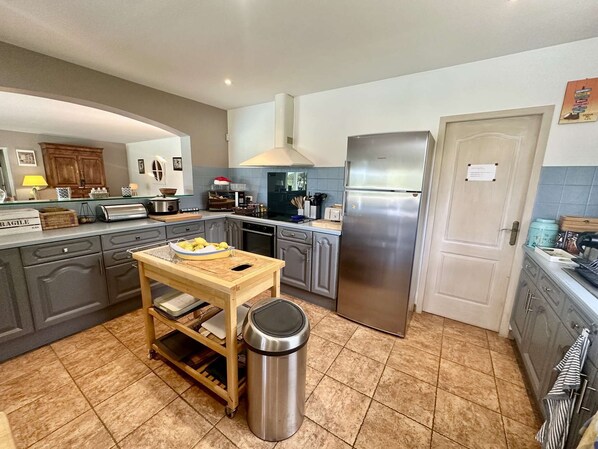 A modern kitchen with grey cabinets, a stainless steel refrigerator, and a wooden island with a trash bin.