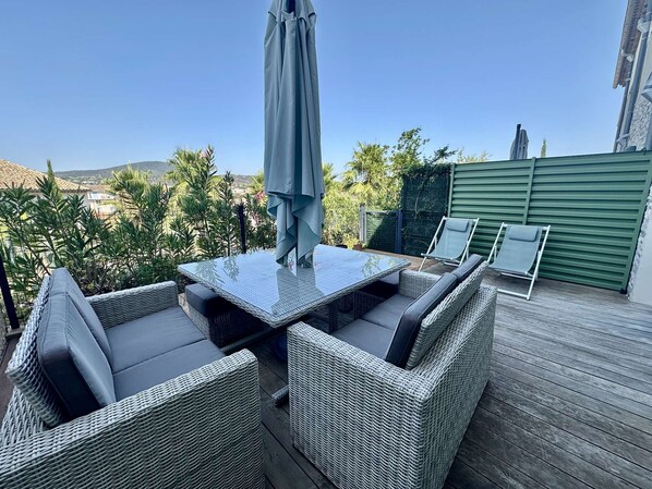 An outdoor patio with a glass-top table and wicker chairs, overlooking a scenic landscape.