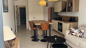A modern kitchen with a wooden countertop, a built-in oven, and a coffee machine. There is a dining area with a wooden table and chairs, and a sofa with a decorative pillow. - Cosy apartment in new residence  (Propriano)