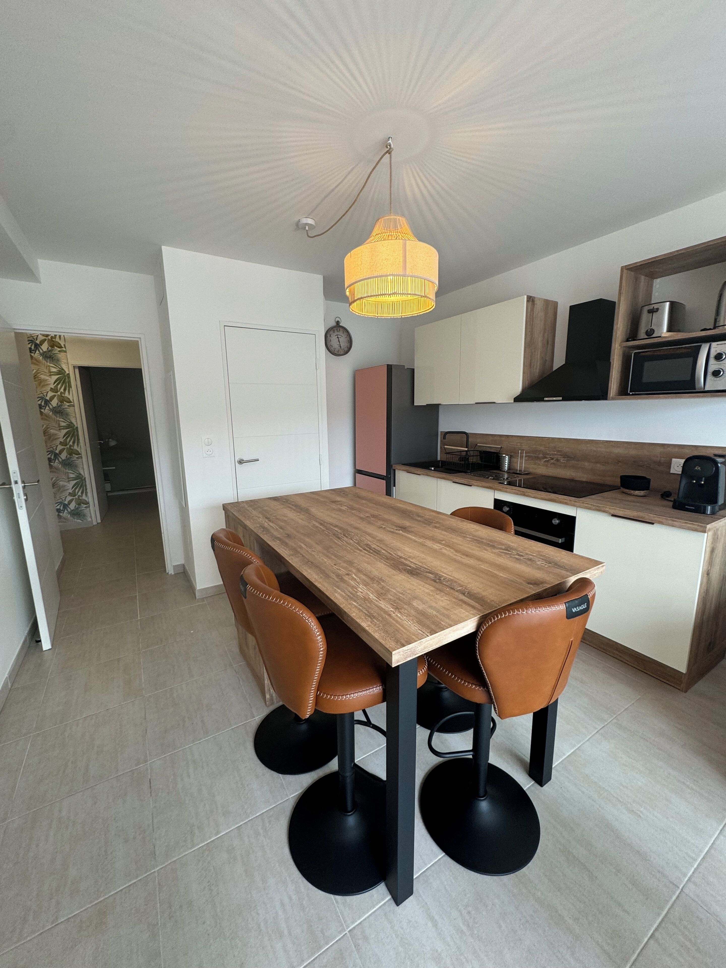 A modern kitchen with a wooden dining table, four chairs, and a hanging light fixture.