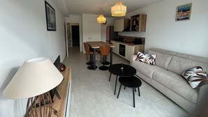 A modern living room with a sofa, coffee table, and dining area. There is a kitchen in the background with wooden cabinets and a microwave. - Cosy apartment in new residence  (Propriano)