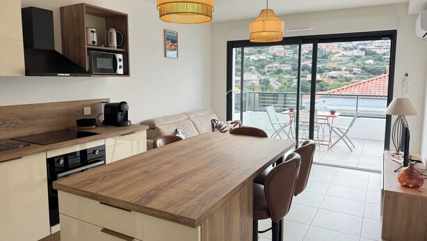A modern kitchen with a central island, wooden cabinets, and a dining area with chairs. - Cosy apartment in new residence  (Propriano)