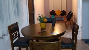 Un coin repas avec une table ronde, quatre chaises en bois, un vase jaune rempli de fleurs et une bouteille d’eau bleue.