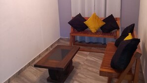 Une petite pièce avec un banc en bois, une table basse et une fenêtre avec des rideaux.