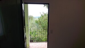 Une porte ouverte donnant sur un balcon doté d’un sol carrelé et d’une rambarde en métal.