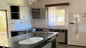 A modern kitchen with a central island, stainless steel appliances, and a window with curtains.