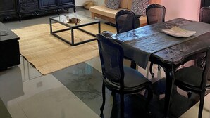 A living room with a sofa, a coffee table, and a dining table with chairs. There is a ceiling fan, a window with curtains, and a wall with framed artwork.