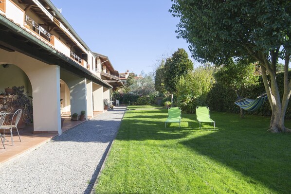 Un patio con un sendero de grava, dos sillas verdes y una hamaca.