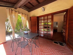Un patio al aire libre con una mesa y sillas, una puerta de madera y vistas al jardín.