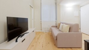 A modern living room with a flat-screen TV on a white stand, a beige sofa, and a wooden floor. - GuestHost - Primaticcio M1 Modern and Bright Apartment (Milano)