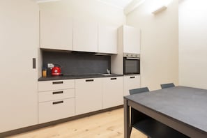 A modern kitchen with a built-in oven, a red kettle, and a dining table with chairs.