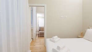 A hotel room with a bed, a small bedside table, a nightstand, and a door leading to another room. - GuestHost - Primaticcio M1 Modern and Bright Apartment (Milano)
