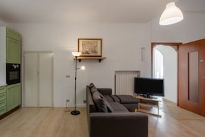 Ein Wohnzimmer mit Sofa, Fernseher, Stehlampe und einem Bild an der Wand.