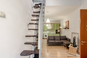 A staircase leading to a living area with a sofa, a television, and a kitchen in the background.
