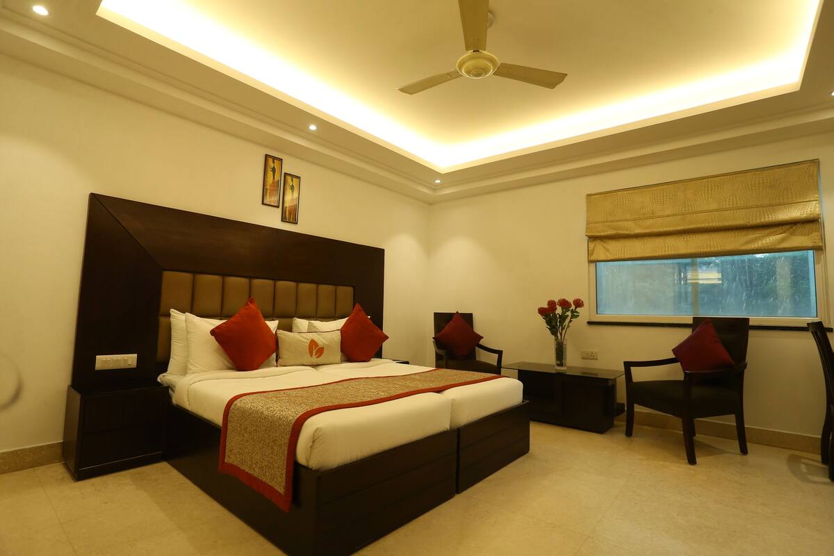 A modern bedroom with a large bed, a ceiling fan, a window with a view, and a small table with flowers.
