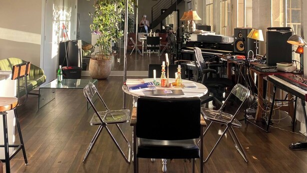Een ruime kamer met een lange tafel, stoelen, een potplant en diverse elektronische apparaten.
