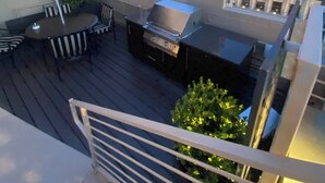 Een terras op het dak met een barbecue, buitenmeubels en een grote gestreepte parasol.