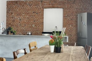 Une cuisine avec un mur en briques, une table à manger en bois avec des chaises et un réfrigérateur.