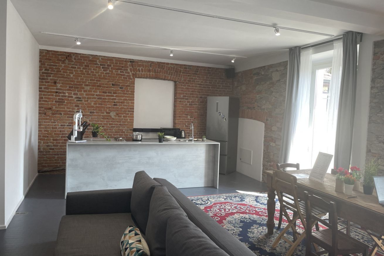 A modern kitchen with a brick wall, a central island, and a dining area with a table and chairs.