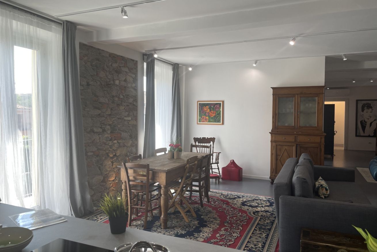 A dining area with a wooden table and chairs, a red rug, and a stone wall.