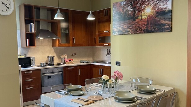 Une cuisine moderne avec des meubles en bois, un four encastré et un coin repas avec une table dressée pour quatre personnes.