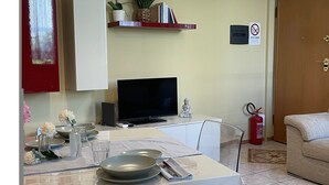 Un coin repas avec une table dressée pour deux personnes, un téléviseur, une bibliothèque et un extincteur.