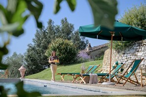 Zona de piscina amb gandules, un mur de pedra i una persona passant.