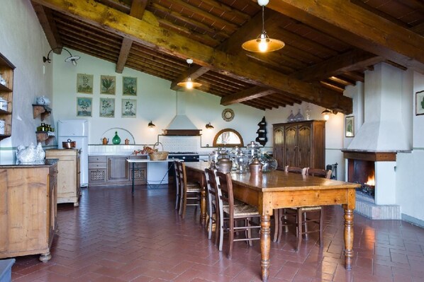 Una cocina rústica con una amplia mesa de madera, lámparas colgantes y una chimenea.