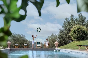 Zona de piscina con sillas de descanso, un jacuzzi y una persona leyendo.