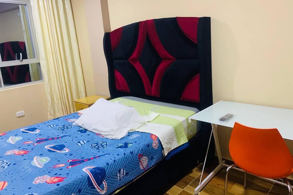Quarto pequeno e bem organizado com uma cama, uma mesa e uma cadeira laranja.