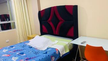 A small, neatly arranged room with a bed, a table, and an orange chair.