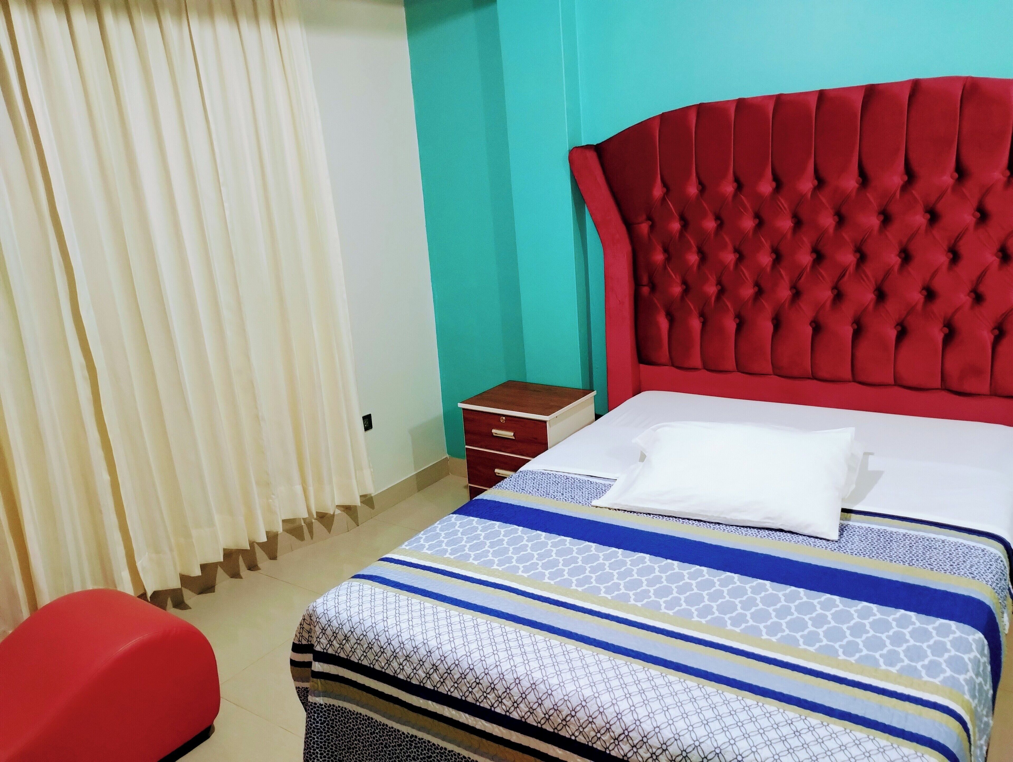 A room with a bed, a red upholstered headboard, a wooden nightstand, and a red bench.
