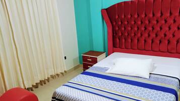 A room with a bed, a red upholstered headboard, a wooden nightstand, and a red bench.