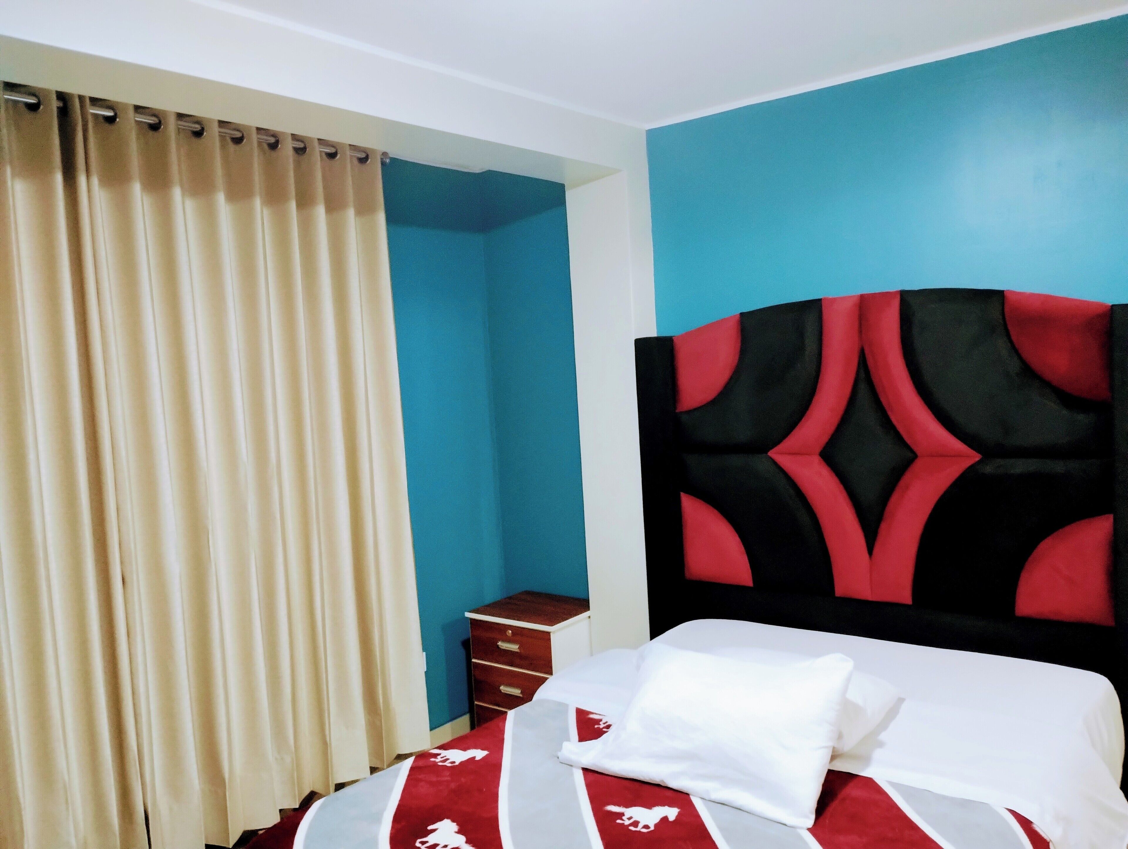 A hotel room with a bed, a nightstand, a drawer, a curtain, and a wall painted in two colors.