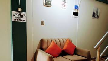 Un sofá color beige con dos cojines naranjas en una habitación con piso de madera a cuadros, una escalera y un letrero en la pared.