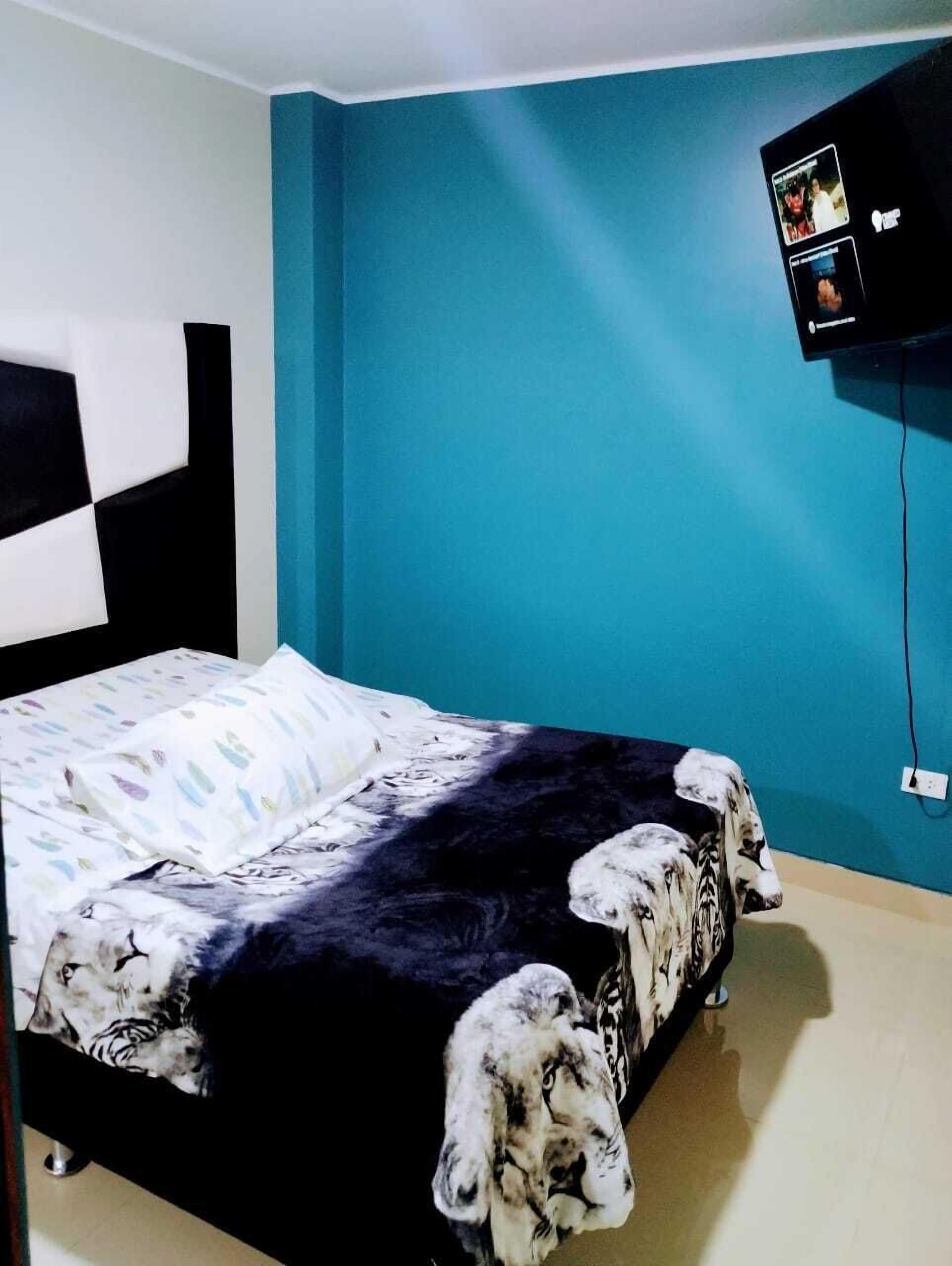 Quarto com cama, televisão presa na parede e parede azul.