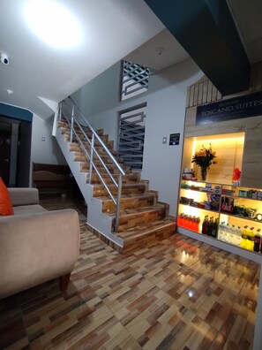 A staircase with wooden steps and metal railings, a reception desk with a sign reading "RECEPCION TOSCANO SUITES", and a display of bottled beverages. - Hostal TOSCANO SUITES  (El Tambo)