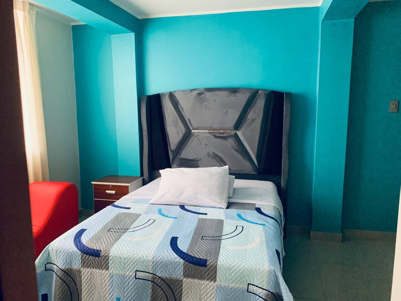 A bedroom with a bed, a nightstand, and a red chair.