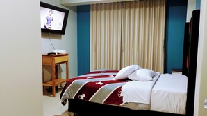 Une chambre d’hôtel avec un lit, un téléviseur fixé au mur, un bureau et un rideau.