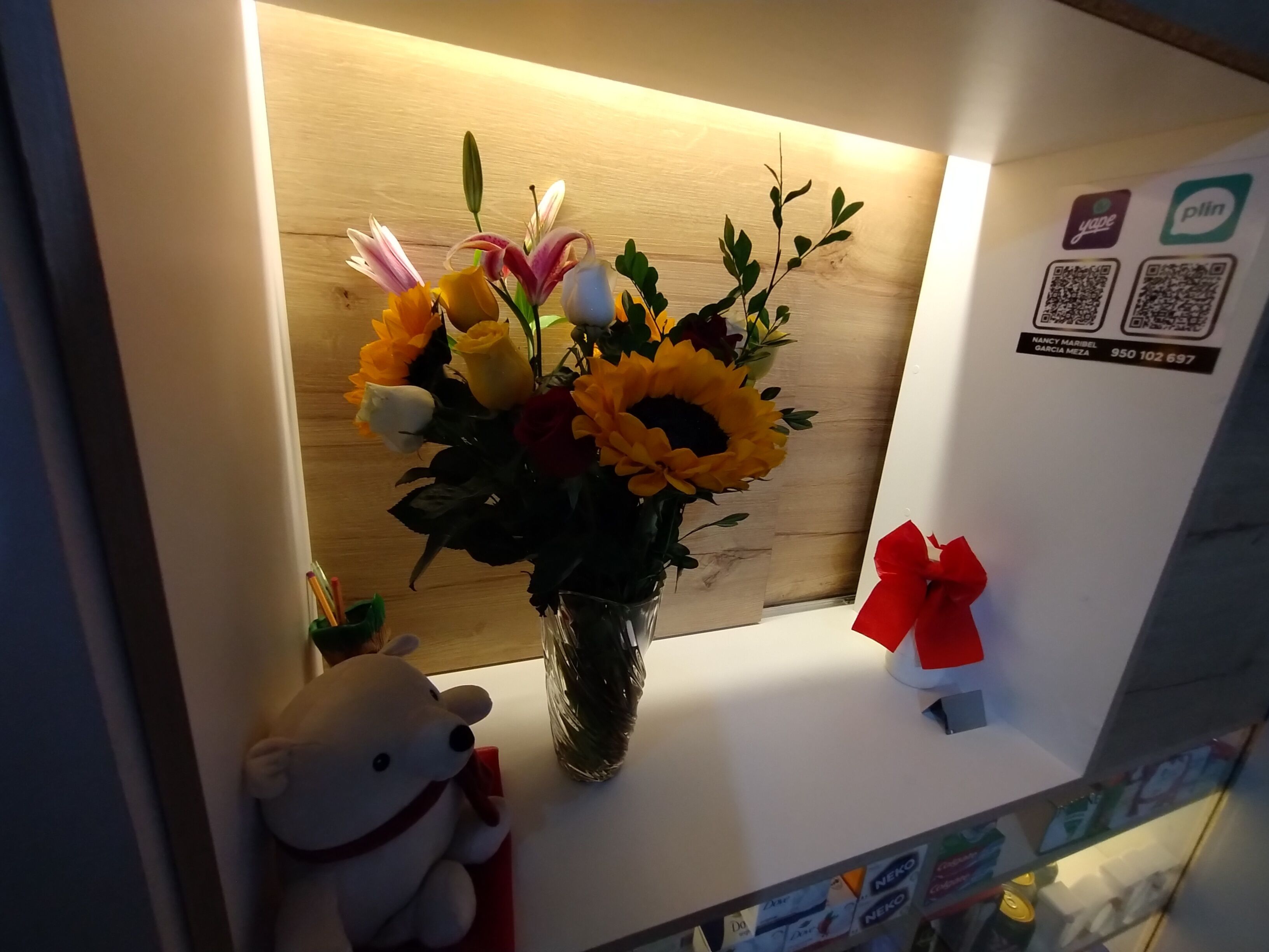 Un mostrador de recepción con un jarrón de flores, un peluche y una caja roja de regalo.