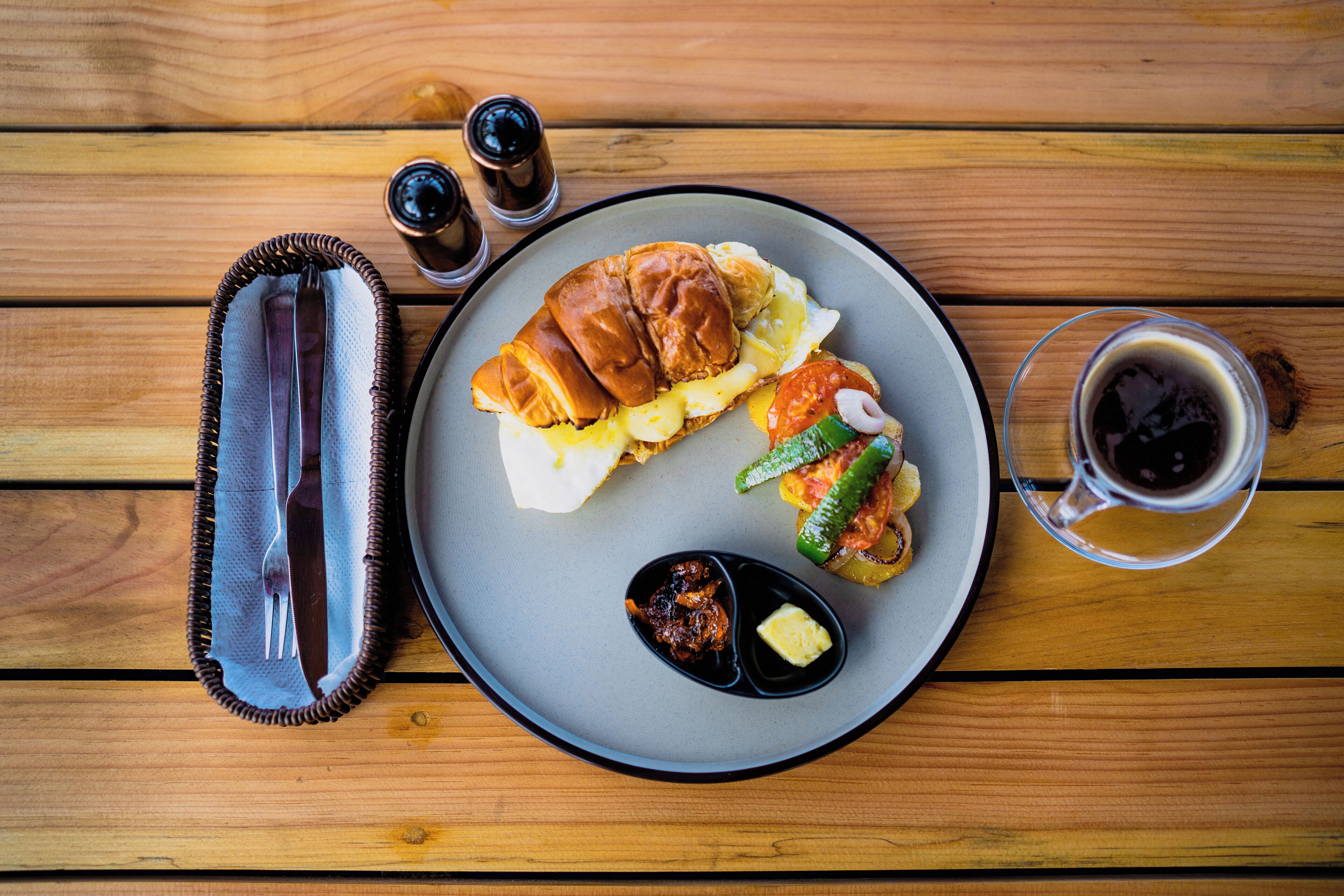 A plate with a sandwich, vegetables, and condiments on a wooden table.