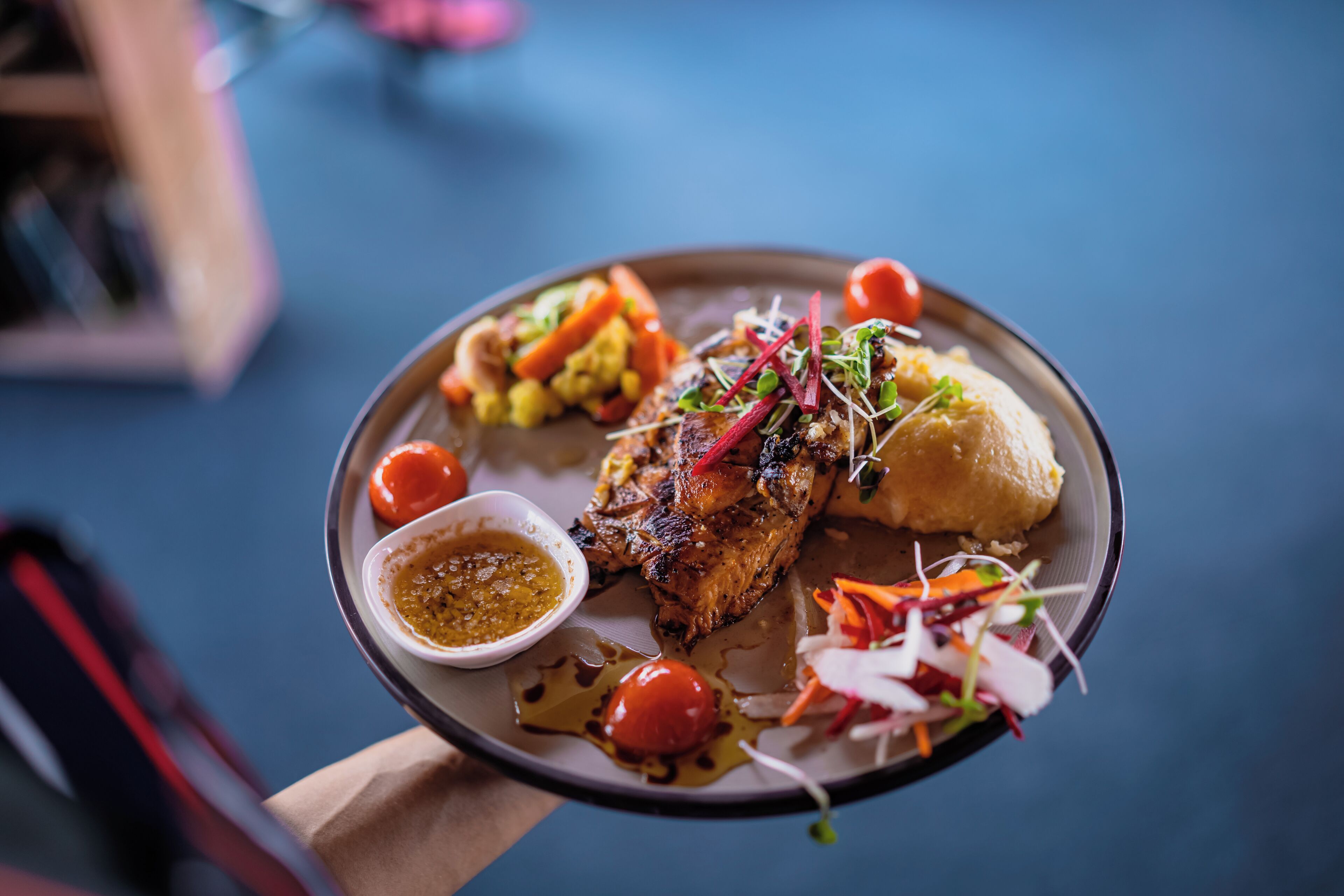 Un plato de comida con carne a la parrilla, verduras y un recipiente pequeño con salsa.